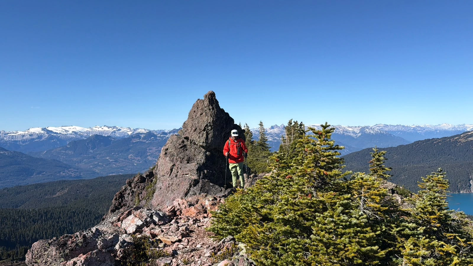 Harpreet Sandhu beside a rocky outcrop on Clinker’s ridge, with forest and distant mountain ranges behind